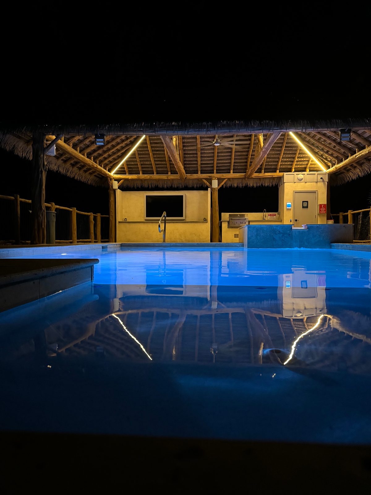Pool and spa glowing under the lit palapa at night
