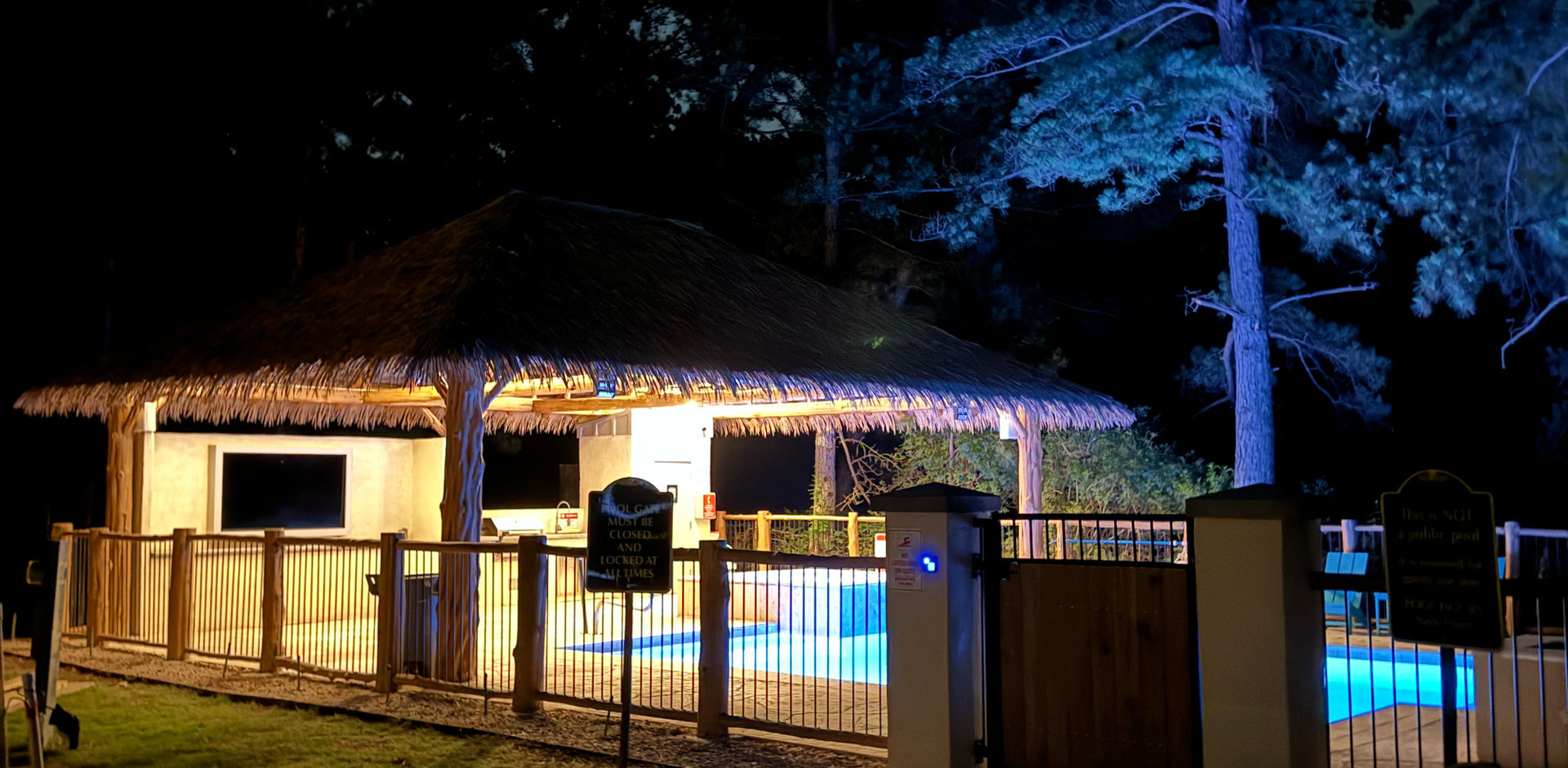 Image of the pool and spa at night showing the palapa lit up.